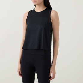 Model wearing Spanx Sheeriours Panel Performance Top in Very Black, with sheer mesh panels, round neck, sleeveless, styled with black leggings.