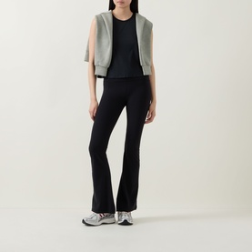 Model wearing Spanx Sheeriours Panel Performance Top in Very Black, paired with grey vest and black flared trousers, white trainers.