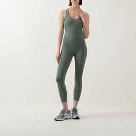 Model wearing Spanx BoostUp Shelf Tank in Eucalyptus with matching cropped leggings and grey trainers.