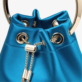 Jimmy Choo bucket bag in lagoon blue satin with light gold ring handle, eyelets, and chain drawstring detail, close-up view.