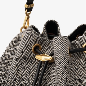Close-up of black and white herringbone tweed bucket bag with gold-tone hardware, drawstring top, and black leather trim detailing