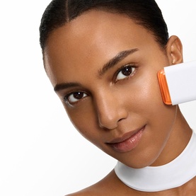 Model with Lanc&ocirc;me UVEX Supra Screen Stick SPF50 applied to cheek, white and orange compact stick format shown in use