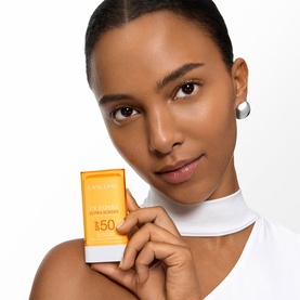 Model with Lanc&ocirc;me UVEX Supra Screen Stick SPF50 held up to face, wearing white top and silver earring