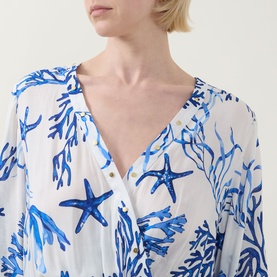 Model wearing Naia Beach Celia La Mer Print Kaftan in white with blue starfish and coral print, V-neckline with gold-tone stud detail visible