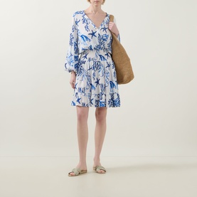 Model wearing Naia Beach Celia La Mer Print Kaftan in blue and white marine print, styled with a straw tote bag and gold flat sandals.