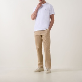 Model wearing white crew neck T-shirt with small chest logo, styled with beige chinos and cream trainers