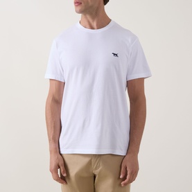 Model wearing white crew neck T-shirt with small dark dog logo embroidery on chest, styled with beige trousers