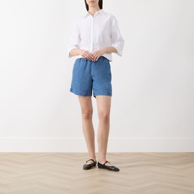 Model wearing Selected Femme Bright White linen-cotton shirt, styled with blue shorts and black flat shoes.