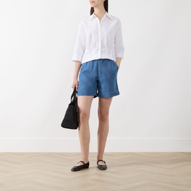 Model wearing Selected Femme Bright White linen-cotton shirt, styled with blue shorts and black ballet flats, carrying a black bag.
