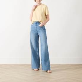 Model wearing Selected Femme Essential Solid T-Shirt in Italian Straw, boxy fit with short sleeves, styled with wide-leg blue jeans and tan sandals.