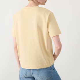 Model wearing Selected Femme Essential Solid T-Shirt in Italian Straw, boxy fit, short sleeves, styled with blue jeans. Back view.