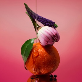 Phlur Paradise Nectar Hair and Body Mist lifestyle shot featuring orange citrus fruit, purple hyacinth and tulip with pink gradient background.