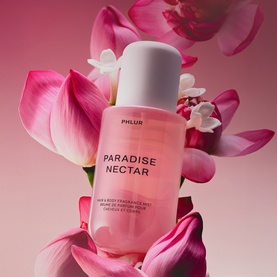 Phlur Paradise Nectar Hair and Body Mist in clear pink bottle, surrounded by pink lotus flowers on rose background