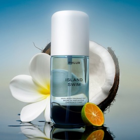 Phlur Island Swim Hair and Body Mist in clear blue bottle, styled with coconut, frangipani flower and citrus fruit