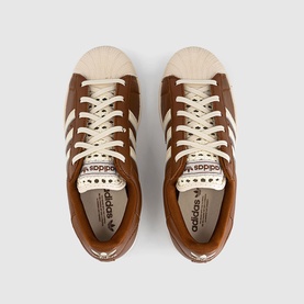 Adidas trainers in Dusky Bronze and Cream White, overhead view showing shell toe cap, three-stripe detail, and cream laces
