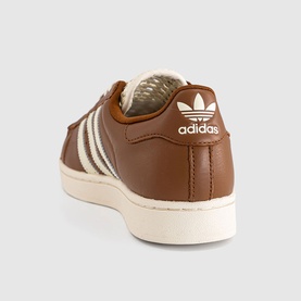 Adidas Superstar trainer in Dusky Bronze, cream white leather upper with shell toe, off-white stripe detail and cream sole, rear view.