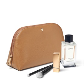 Aspinal of London caramel leather makeup bag with gold zip, styled with a makeup brush, lipstick, and fragrance bottle.