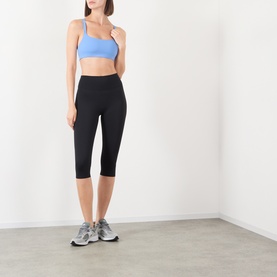 Model wearing Adanola black cropped high-waist leggings with a blue sports bra and grey trainers.