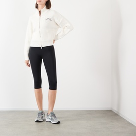 Model wearing Adanola black cropped leggings, styled with a white zip-up jacket and grey trainers.