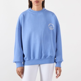 Model wearing Adanola Blossom Blue cotton sweat top with small chest graphic, styled with white trousers