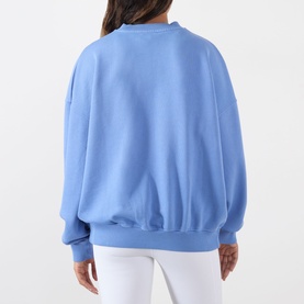 Model wearing Adanola Blossom Blue cotton sweat top, rear view, styled with white trousers