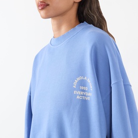 Model wearing Adanola Blossom Blue cotton sweat top with crew neck and embroidered chest logo graphic detail.