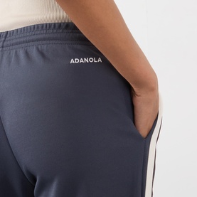 Model wearing Adanola Midnight Blue Sweat Bottoms, close-up of back pocket and contrast side stripe detail, white top visible above waistband.