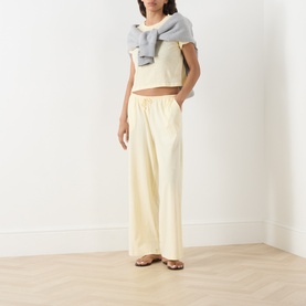 Model wearing Adanola ButterCream cotton T-shirt, styled with wide-leg trousers, grey knit top draped over shoulders and tan sandals.