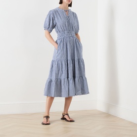 Model wearing Barbour Ashwell Gingham Tiered Dress in Multi Gingham with puff sleeves and tiered midi skirt, styled with brown strappy sandals