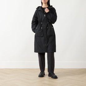 Model wearing Barbour International black longline hooded jacket with drawstring waist, styled with dark trousers and black chunky loafers.