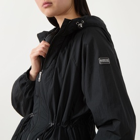 Model wearing Barbour International black hooded jacket with zip fastening, drawstring waist, and branded woven badge on sleeve.