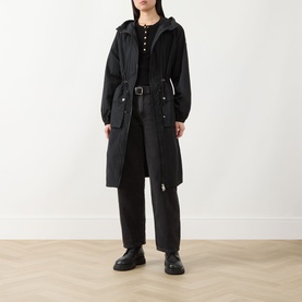 Model wearing Barbour International black hooded belted longline jacket, styled with black wide-leg trousers and black chunky loafers.
