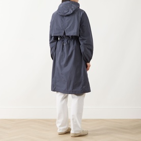 Model wearing Barbour International jacket in Odyssey blue, rear view showing hood, cinched waist, and midi length, styled with white trousers