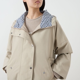 Model wearing Barbour Kingswood Showerproof Jacket in Light Sand with navy gingham lined hood, snap button placket, styled over a striped top.