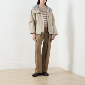 Model wearing Barbour Kingswood Showerproof Jacket in Light Sand with Navy Gingham hood, styled with striped top, brown wide-leg trousers and black