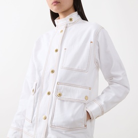 Model wearing Barbour International Kyla Biker Denim Jacket in Denim White with gold buttons, contrast stitching, and oversized flap pockets.