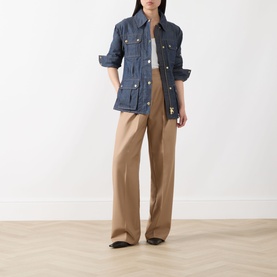 Model wearing Barbour International International Denim Trench Jacket in dark blue with gold-tone hardware, styled with wide-leg tan trousers.