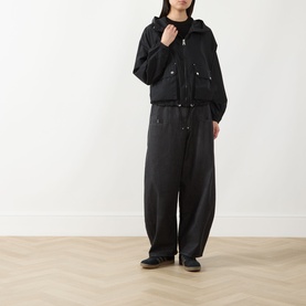 Model wearing Barbour International black hooded jacket with drawstring hem, styled with wide-leg black trousers and dark flat shoes.