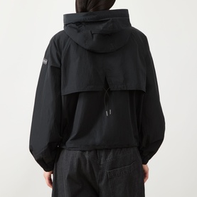 Model wearing Barbour International black hooded jacket, back view, styled with matching black trousers. Woven badge on sleeve.