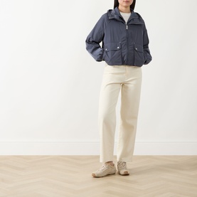 Model wearing Barbour International Maizy Showerproof Jacket in Odyssey blue-grey with cream trousers and beige trainers.