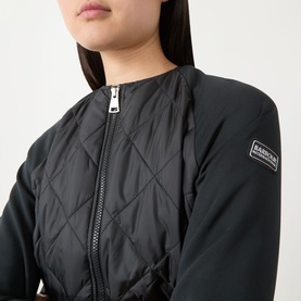 Model wearing Barbour International Seren Quilted Bomber Jacket in black, showing collarless neckline, front zip and quilted panel detail.