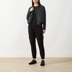 Model wearing Barbour International Seren Quilted Bomber Jacket in black, styled with black jumpsuit and black lace-up shoes.