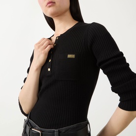 Model wearing Barbour International Kyla Logo Rib-Knit Sweater in black, showing henley neckline, gold branded hardware, and logo badge detail.