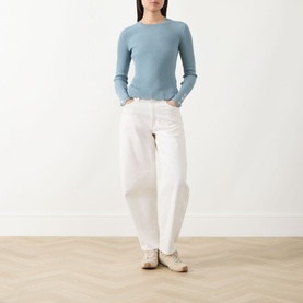 Model wearing Barbour International Seren Rib-Knit Sweater in Washed Pearl Blue with white wide-leg jeans and cream trainers.