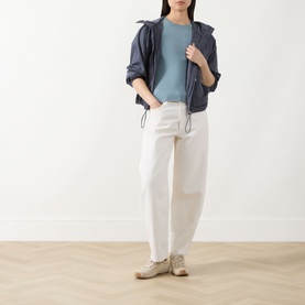 Model wearing Barbour International Seren Rib-Knit Sweater in Washed Pearl Blue, styled with navy zip-up jacket, white trousers and beige trainers.