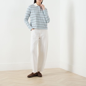 Model wearing Barbour Ashwell Logo Striped Polo Shirt in Celestial Blue Stripe with white wide-leg trousers and brown loafers.