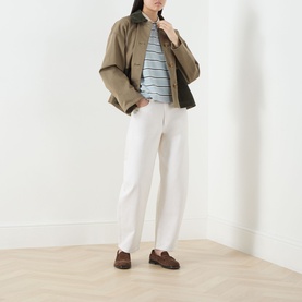 Model wearing Barbour Ashwell Logo Striped Polo Shirt in Celestial Blue Stripe, styled with khaki jacket, white trousers and brown loafers.