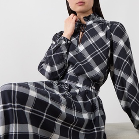 Model wearing Barbour Bailton Tartan Blouse in Dark Navy/White Check with ruffle tie collar, long blouson sleeves, styled with matching tartan