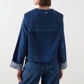 Model wearing Barbour Dartmoor Denim Shirt in Mid Wash Indigo, back view showing shawl collar, long sleeves and turned-up cuffs, styled with blue