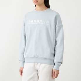 Model wearing Barbour International pearl blue cotton crew neck sweatshirt with white logo print, styled with white trousers.
